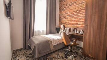 A hotel room with a bed, a desk, a chair, a wardrobe, and a brick wall.