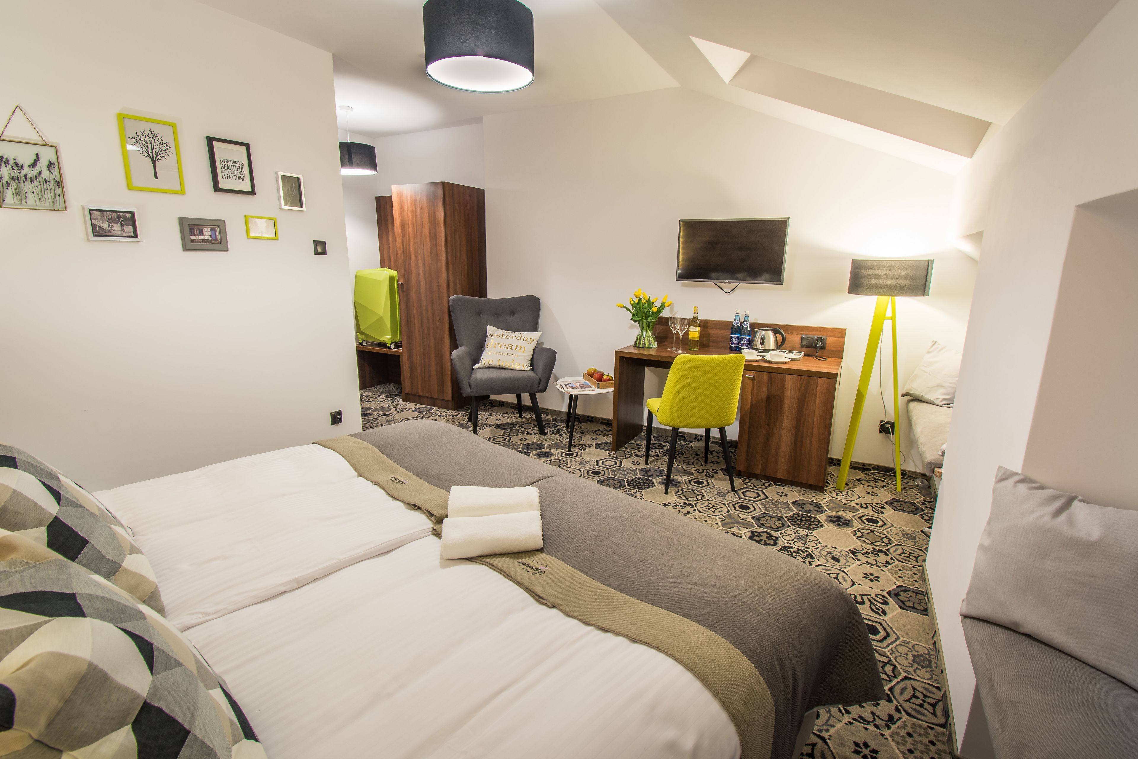 A hotel room with two beds, a desk, a chair, a TV, and a lamp.