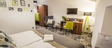 A hotel room with two beds, a desk, a chair, a TV, and a lamp.