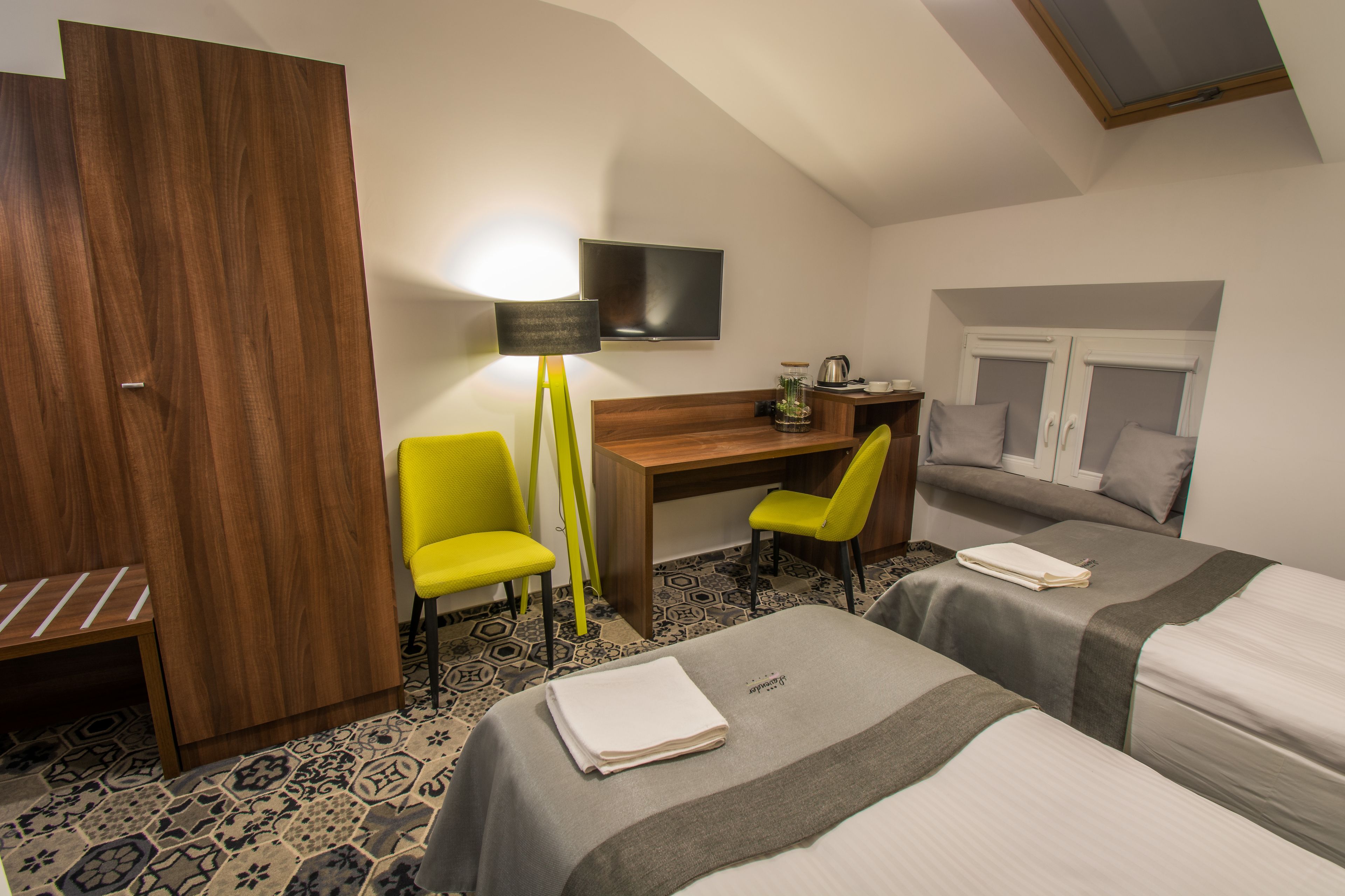 A hotel room with a desk, two chairs, a TV, a bed, and a wardrobe.