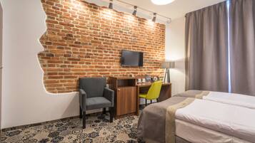 Hotellihuone, jossa on tiiliseinä, taulutelevisio, työpöytä tuolilla, sänky ja kuviollinen lattia.