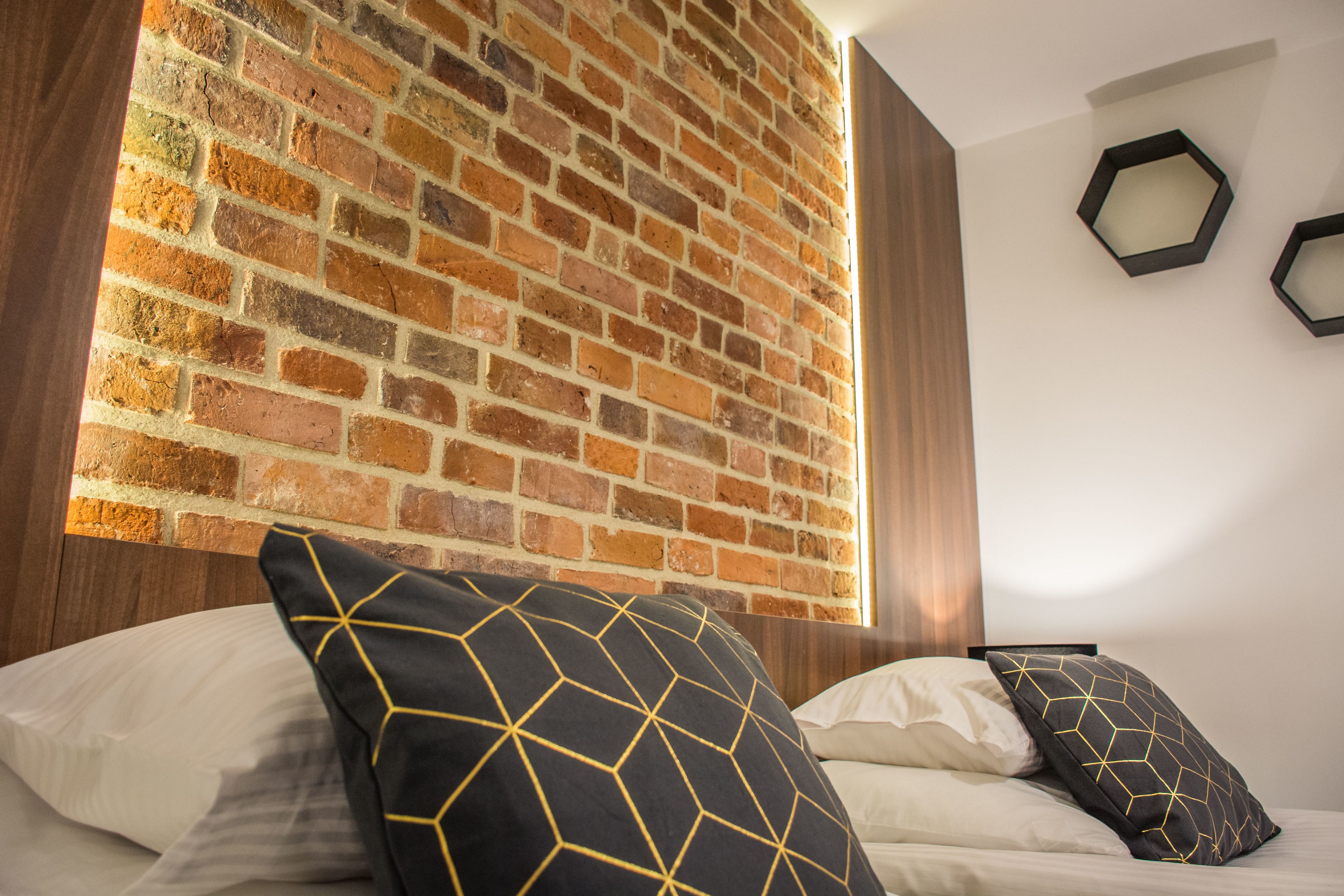 A bedroom with a brick wall, a bed with white and black pillows, and two hexagonal wall decorations.