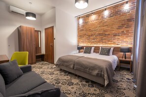 A modern bedroom with a brick wall, a large bed with multiple pillows, a wooden wardrobe, a bright yellow chair, and a patterned carpet. - Hotel Lavender (Kraków)