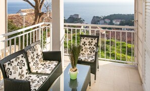 A balcony with wicker furniture, a potted plant, and a view of the sea and buildings. - Apartments Carmelitta (Dubrovnik)