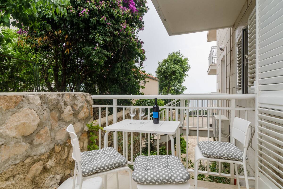 A balcony with a table and two chairs, a bottle of wine, and a stone wall.