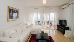 A modern living room with a white sofa, a red rug, a black coffee table with a plant, a black TV stand, and a painting on the wall. - Apartments Carmelitta (Dubrovnik)