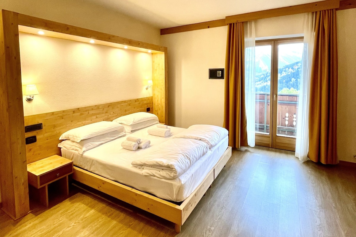Una habitación de hotel con una cama de madera, una mesita de noche y un ventanal con cortinas.