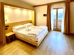 Una habitación de hotel con una cama de madera, una mesita de noche y un ventanal con cortinas.
