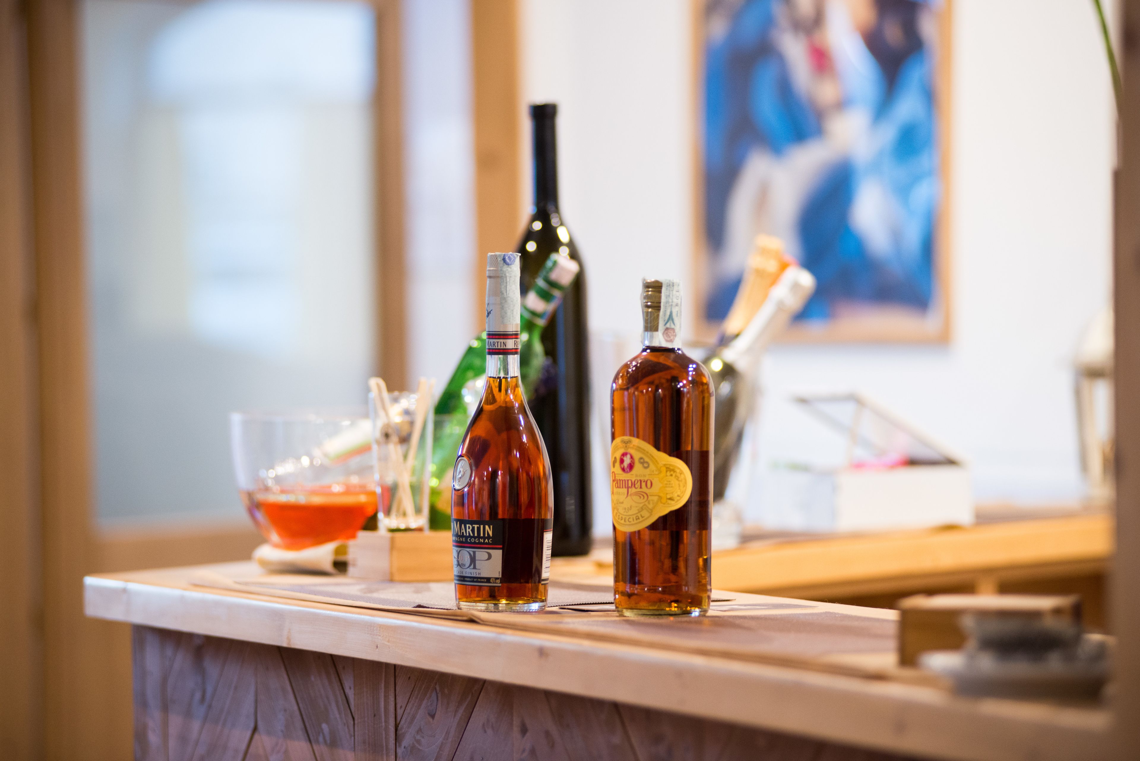 Un espace bar avec des bouteilles d’alcool et un verre d’une boisson rouge sur un comptoir en bois.