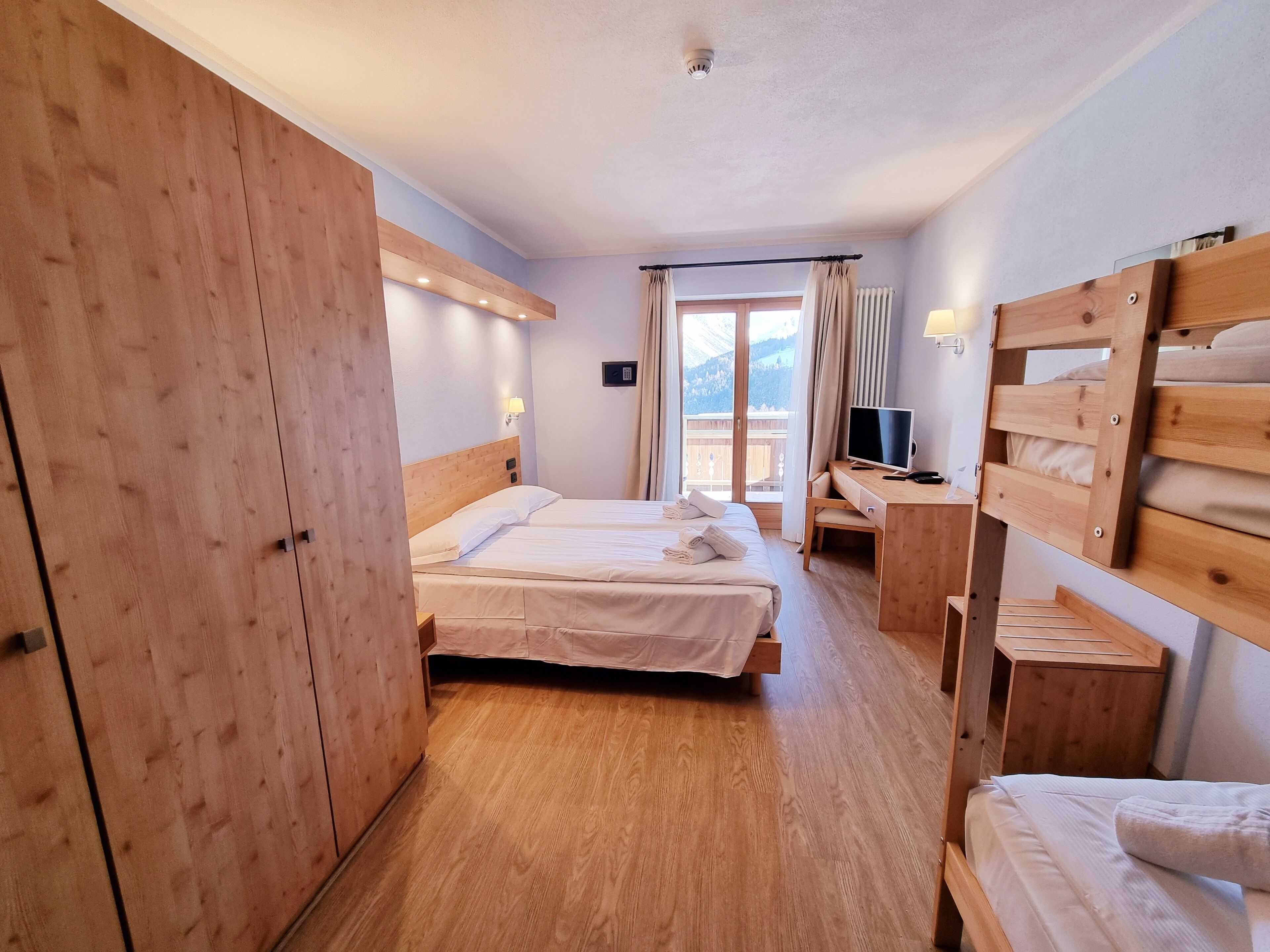 Une chambre d’hôtel avec deux lits, des meubles en bois, un bureau avec un ordinateur et une vue sur l’extérieur.