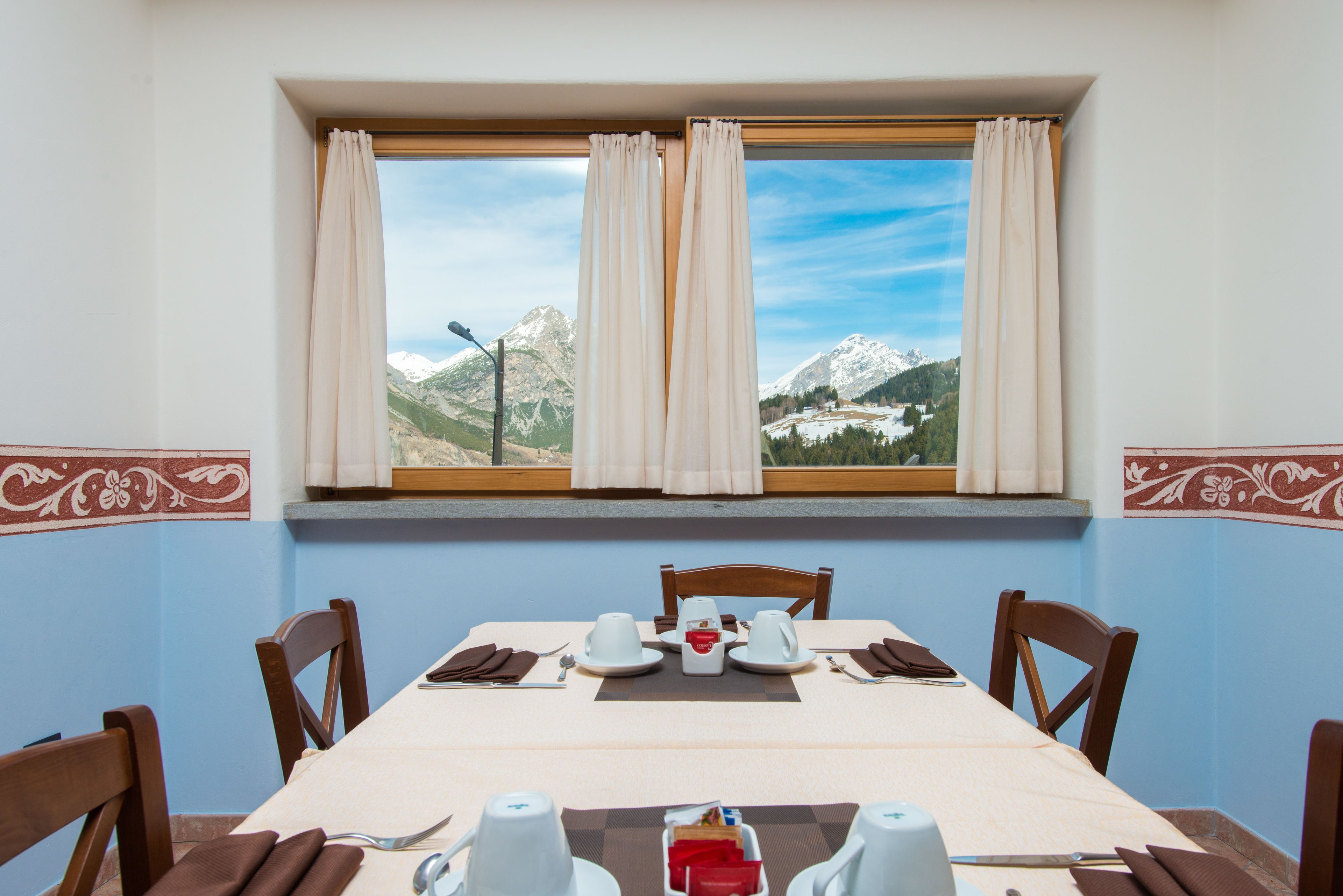 Een eettafel gedekt voor twee personen, met uitzicht op een berg door een raam.
