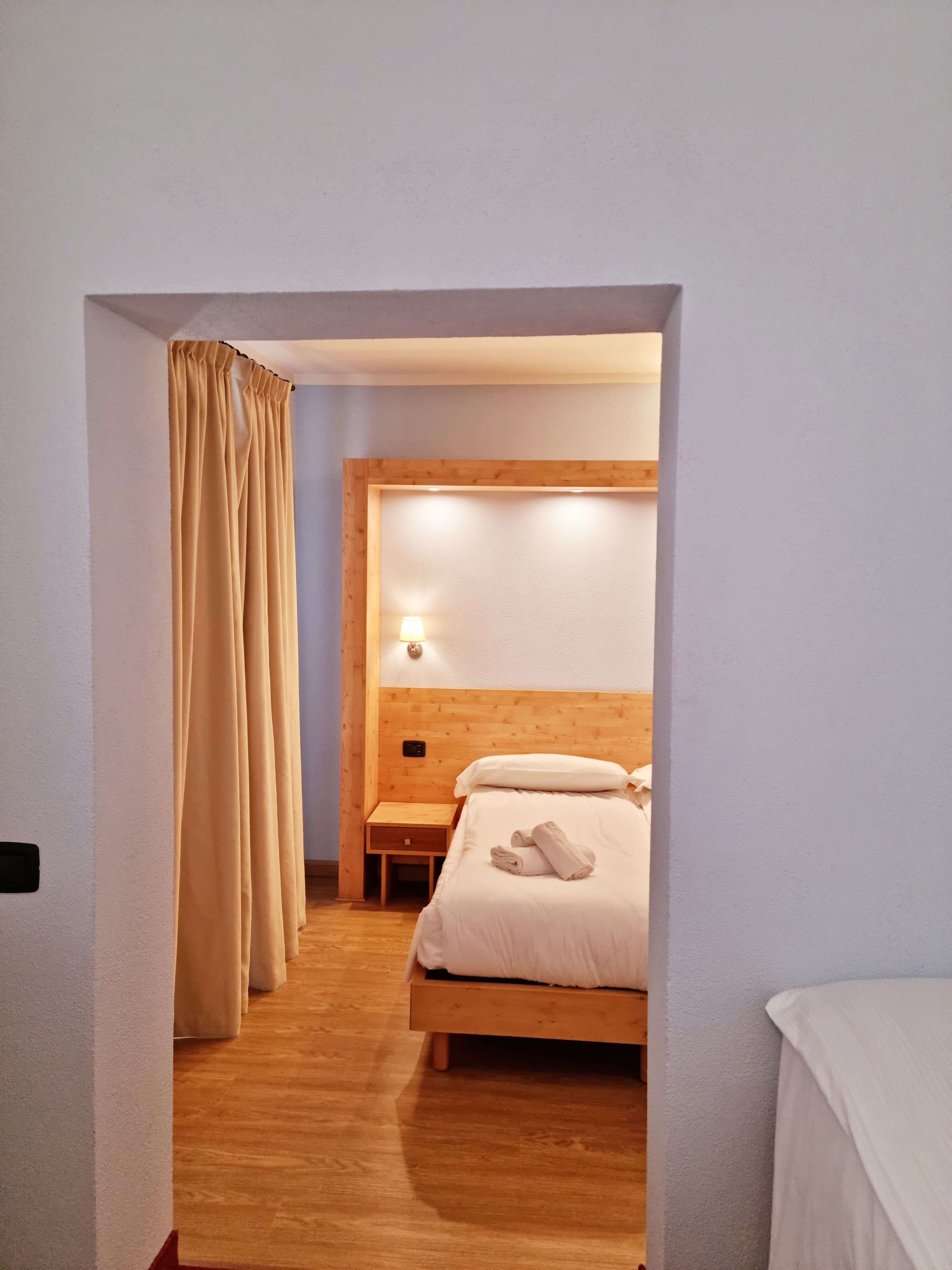 A hotel room with a wooden bed, a nightstand, a lamp, and a curtain.