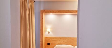 A hotel room with a wooden bed, a nightstand, a lamp, and a curtain.