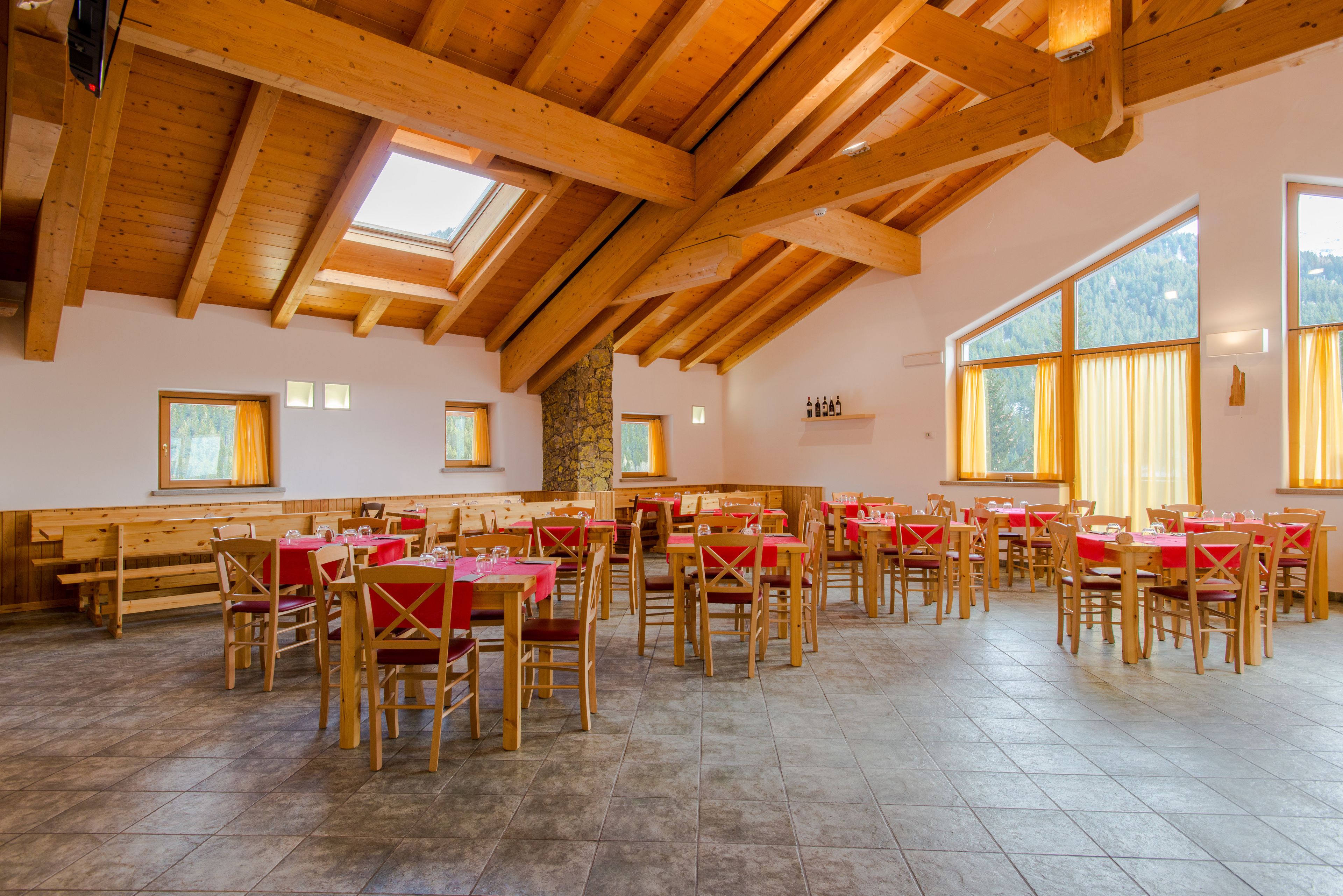 Un comedor espacioso con vigas de madera, ventanas amplias y manteles rojos.