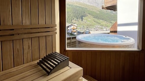 Een houten sauna met raam, met uitzicht op een bergachtig landschap en een whirlpool.