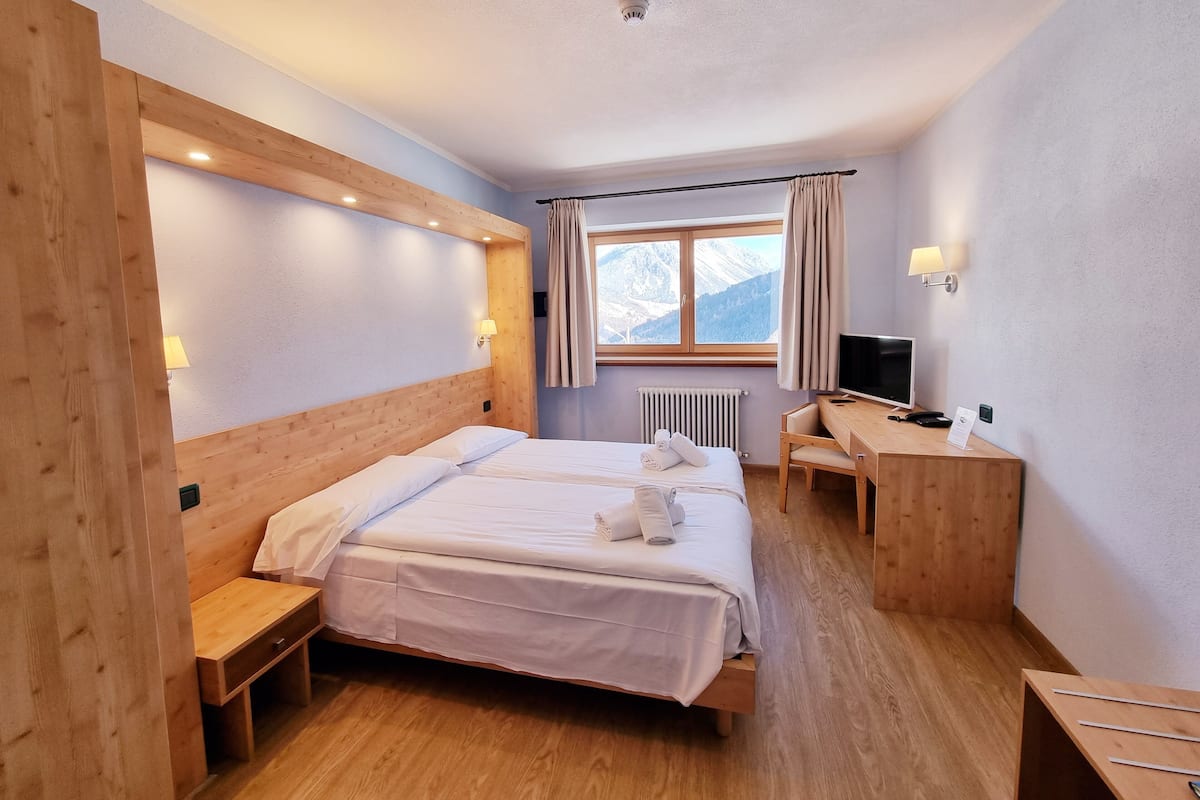 Habitación de hotel con una cama de madera, un escritorio, una silla, un televisor y una ventana con vista a la montaña.
