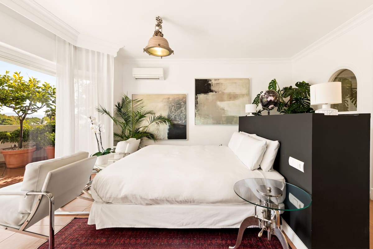 Une chambre d’hôtel moderne avec un grand lit, une table en verre, une chaise et une vue sur l’extérieur.