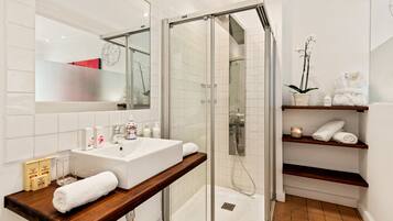 A modern bathroom with a glass-enclosed shower, a white sink, and wooden shelves holding towels and toiletries.