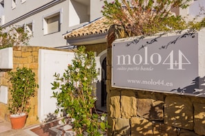 Letrero de 'molo44' con una dirección web, un muro de piedra y plantas en macetas.