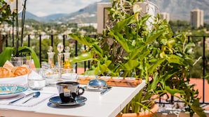 A table set for breakfast with croissants, coffee, and condiments, overlooking a mountainous landscape.