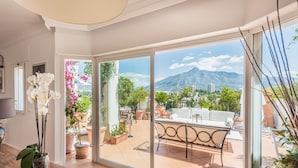 A spacious room with a large sliding glass door leading to an outdoor patio area. The patio features a white outdoor sofa and multiple potted plants.