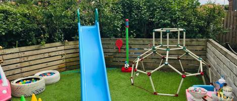 Un área de juegos infantiles con un tobogán azul, una estructura para escalar y un foso de neumáticos.