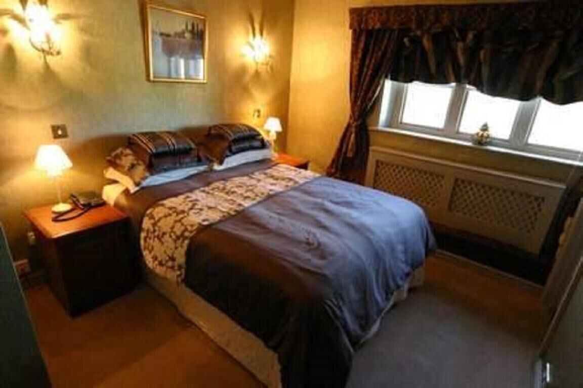 A bedroom with a bed, bedside tables, a lamp, a window with curtains, and a wall-mounted light fixture.