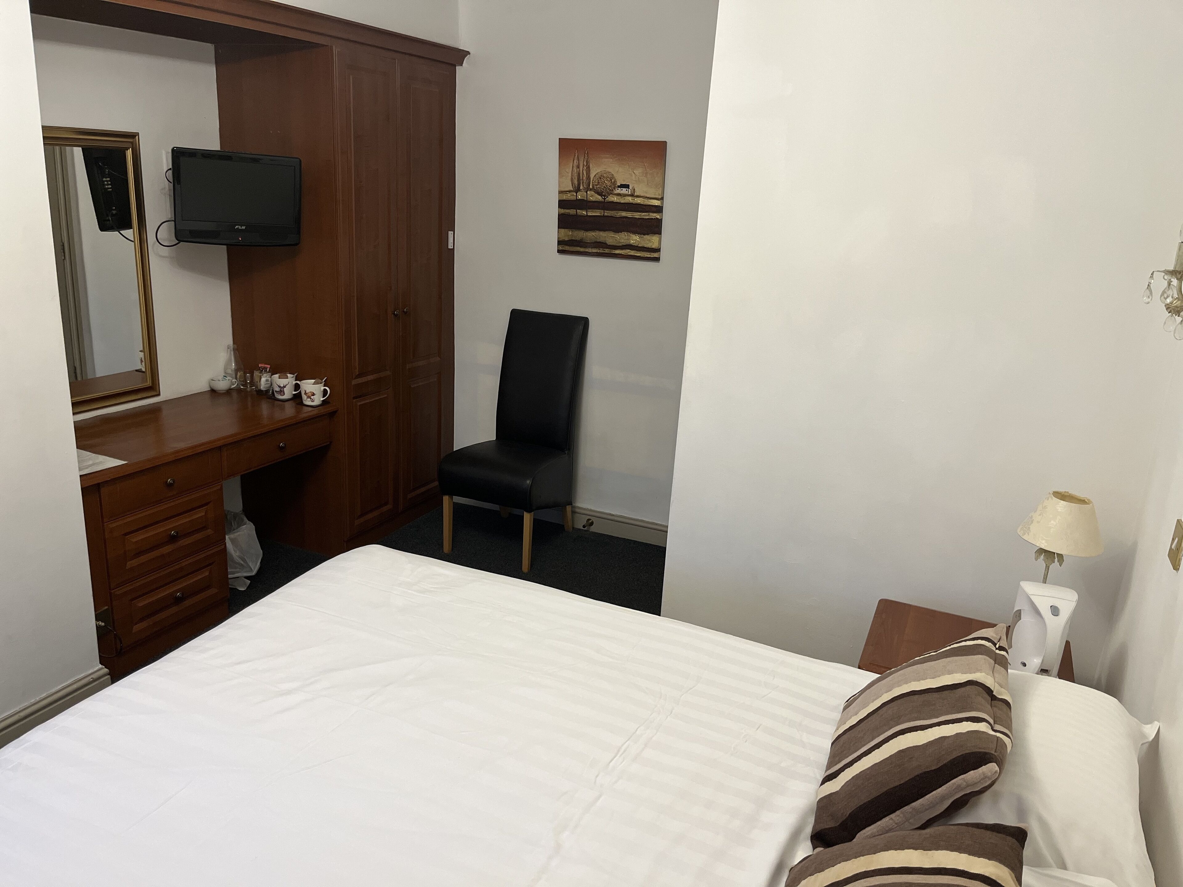 A hotel room with a bed, a wooden desk, a chair, a television, and a painting on the wall.