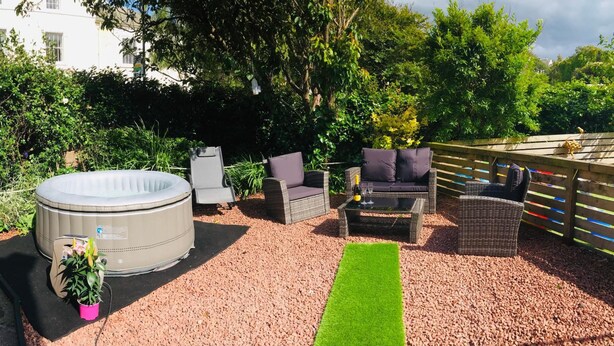 A patio area with a hot tub, wicker furniture, and a small garden.