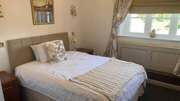 Quarto com cama, mesas de cabeceira, janela com cortinas, radiador e um quadro na parede.