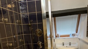 A bathroom with a glass-enclosed shower, a pedestal sink, and a window with blinds.