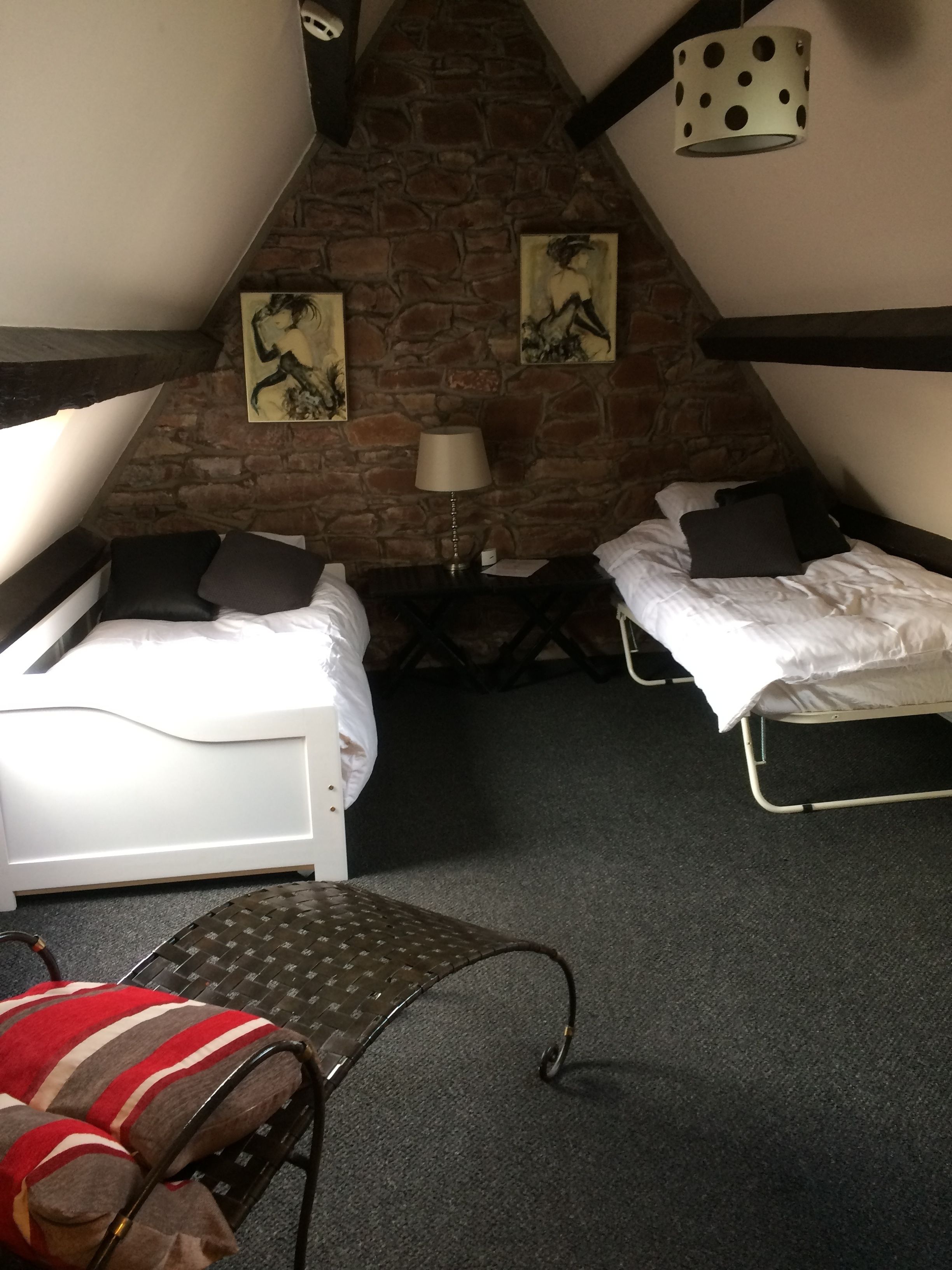 A small, cozy room with two single beds, a stone wall, and a hanging lamp.