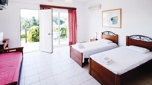 Une chambre d’hôtel avec deux lits en bois, un canapé rouge, une porte-fenêtre coulissante donnant sur l’extérieur et un tableau encadré au mur.