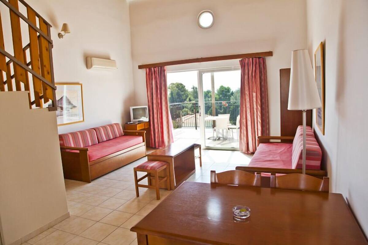 A hotel room with a wooden staircase, a sofa, a dining table, and a balcony with curtains.