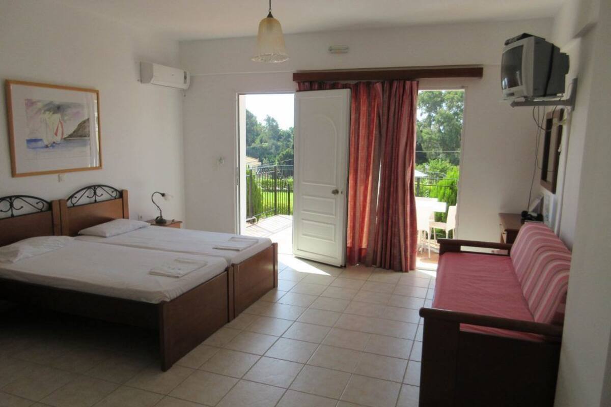 A bedroom with a large bed, a smaller bed, a sofa, a TV, and a balcony with curtains.