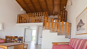 Un grand espace de vie comprenant un escalier en bois, une table à manger avec des chaises, un canapé et un coin cuisine.
