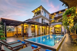 A modern hotel with a swimming pool, outdoor seating, and a covered patio area. - Serene River Villa (Da Nang)