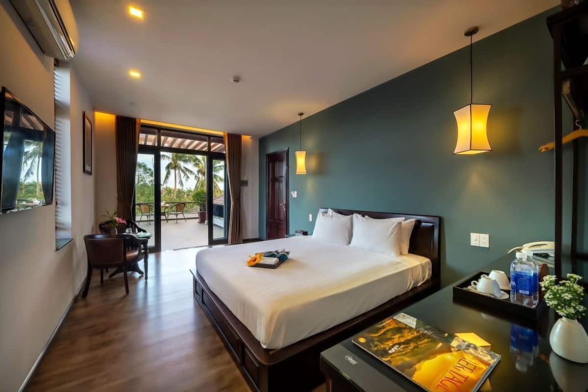 Ein Hotelzimmer mit einem großen Bett, einem Schreibtisch mit Stuhl, einem Esstisch und Blick auf Palmen durch die Glasdoor.