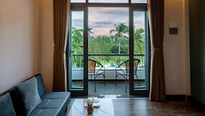 Una habitación con un sofá, una mesita de centro y vistas a un balcón con sillas y una piscina.