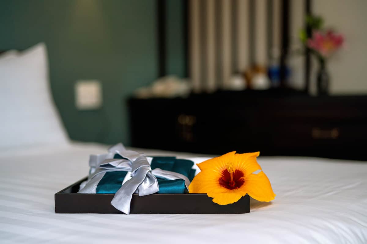 Ein ordentlich gemachtes Bett mit einer Geschenkbox und einer einzelnen Blume darauf.