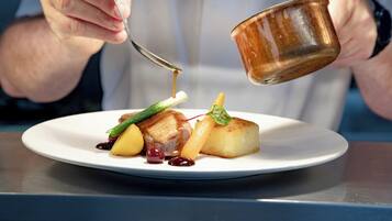 A person pouring a sauce from a small metal cup onto a plate with food.