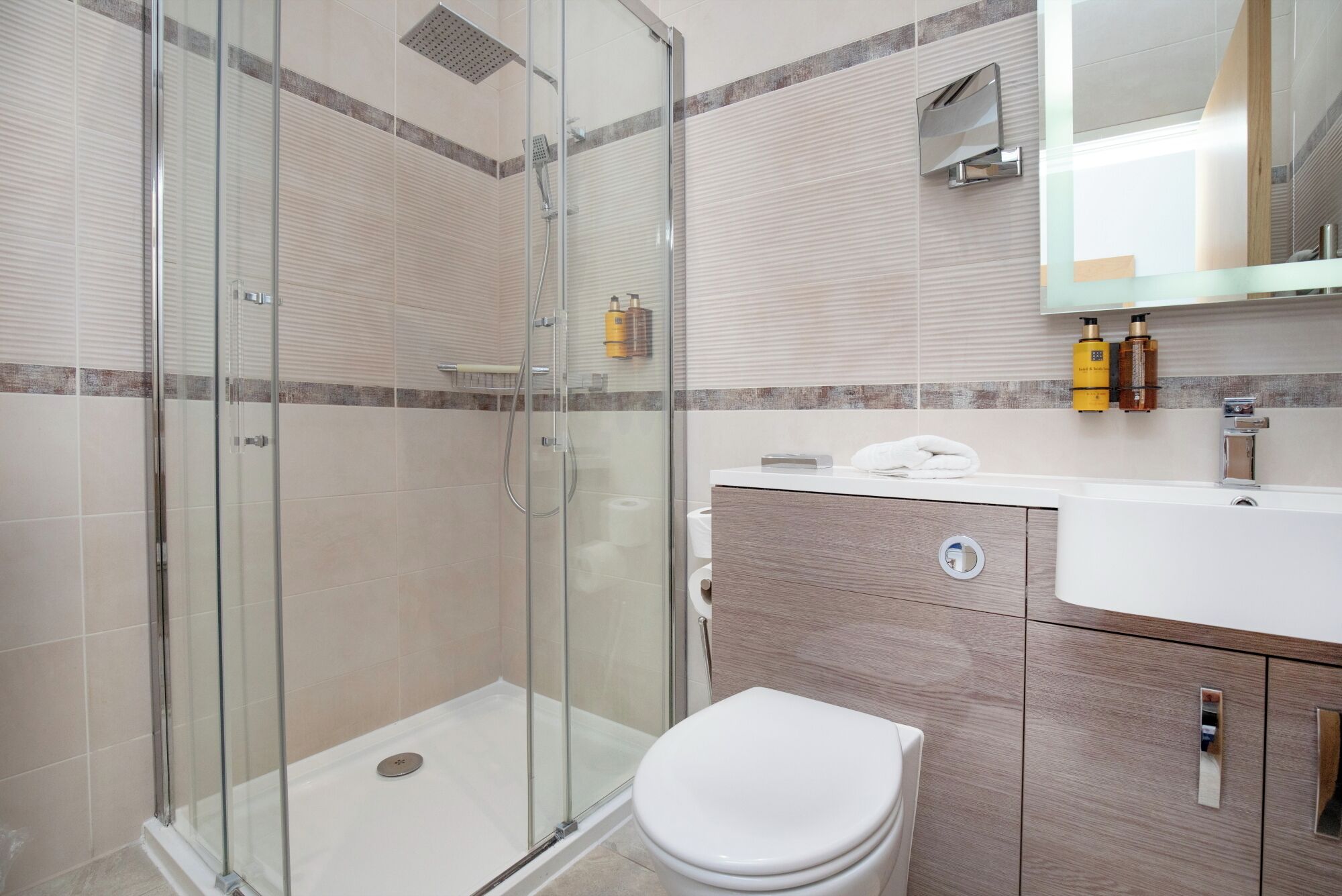 Un baño moderno con cabina de ducha de vidrio, inodoro y tocador con espejo.