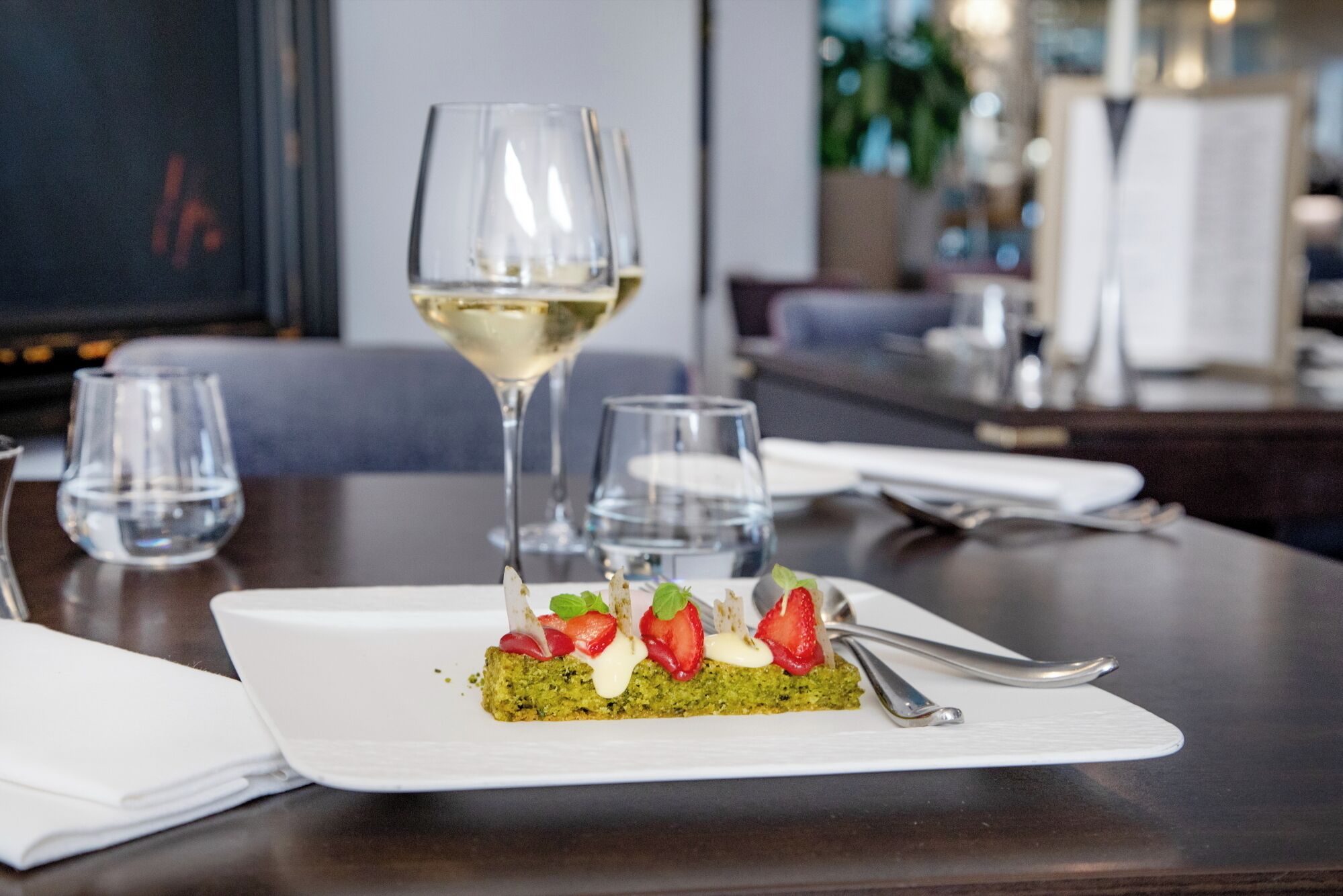 A dessert on a white plate with a glass of white wine and water on a table.