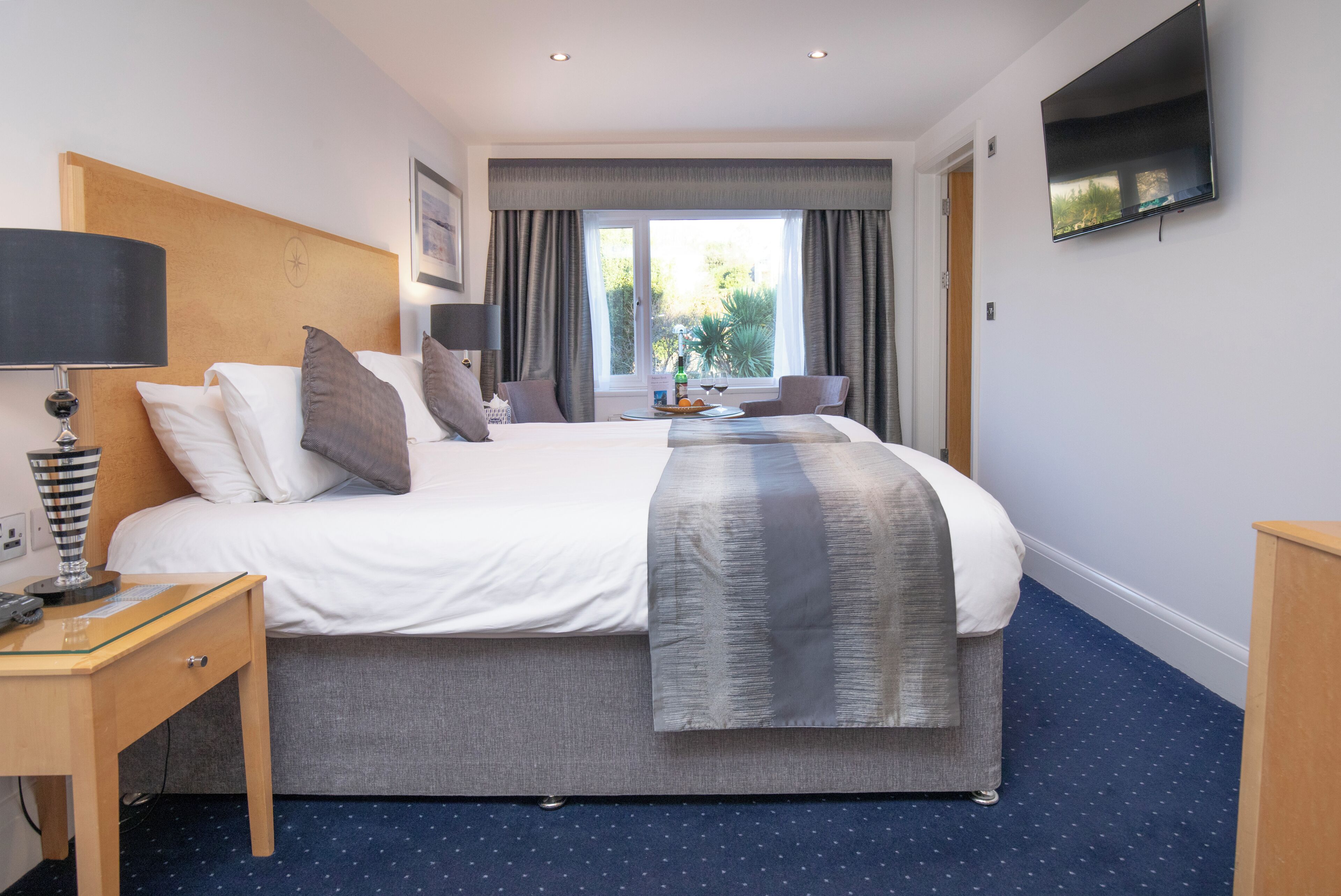 A hotel room with a bed, bedside table, lamp, and a flat-screen TV mounted on the wall.