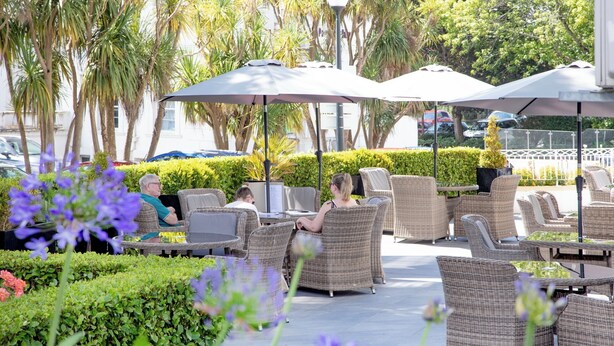 An outdoor seating area with wicker chairs and umbrellas, surrounded by greenery and palm trees. - Belgrave Sands Hotel & Spa (Torquay)
