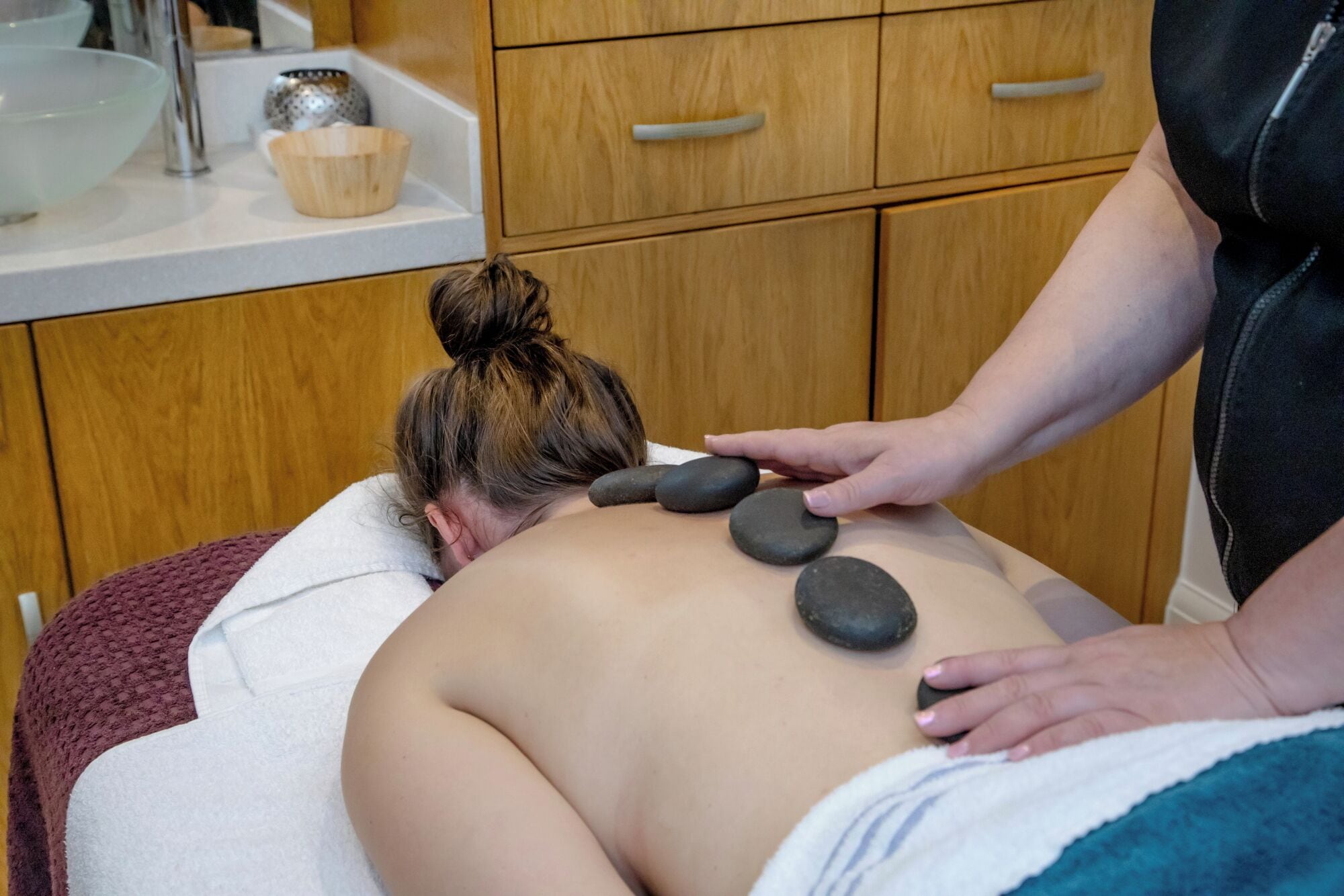 A massage therapy session with a person lying face down, receiving back rubs from another individual.