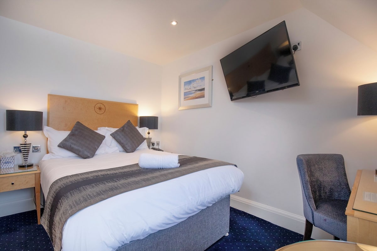 A hotel room with a bed, a desk, a chair, a TV, and a picture on the wall.