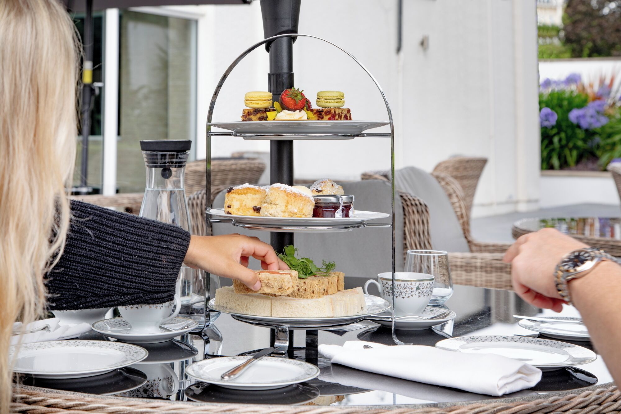 A three-tiered dessert stand with pastries and a sandwich at a table with tea cups and plates.