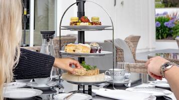A three-tiered dessert stand with pastries and a sandwich at a table with tea cups and plates.