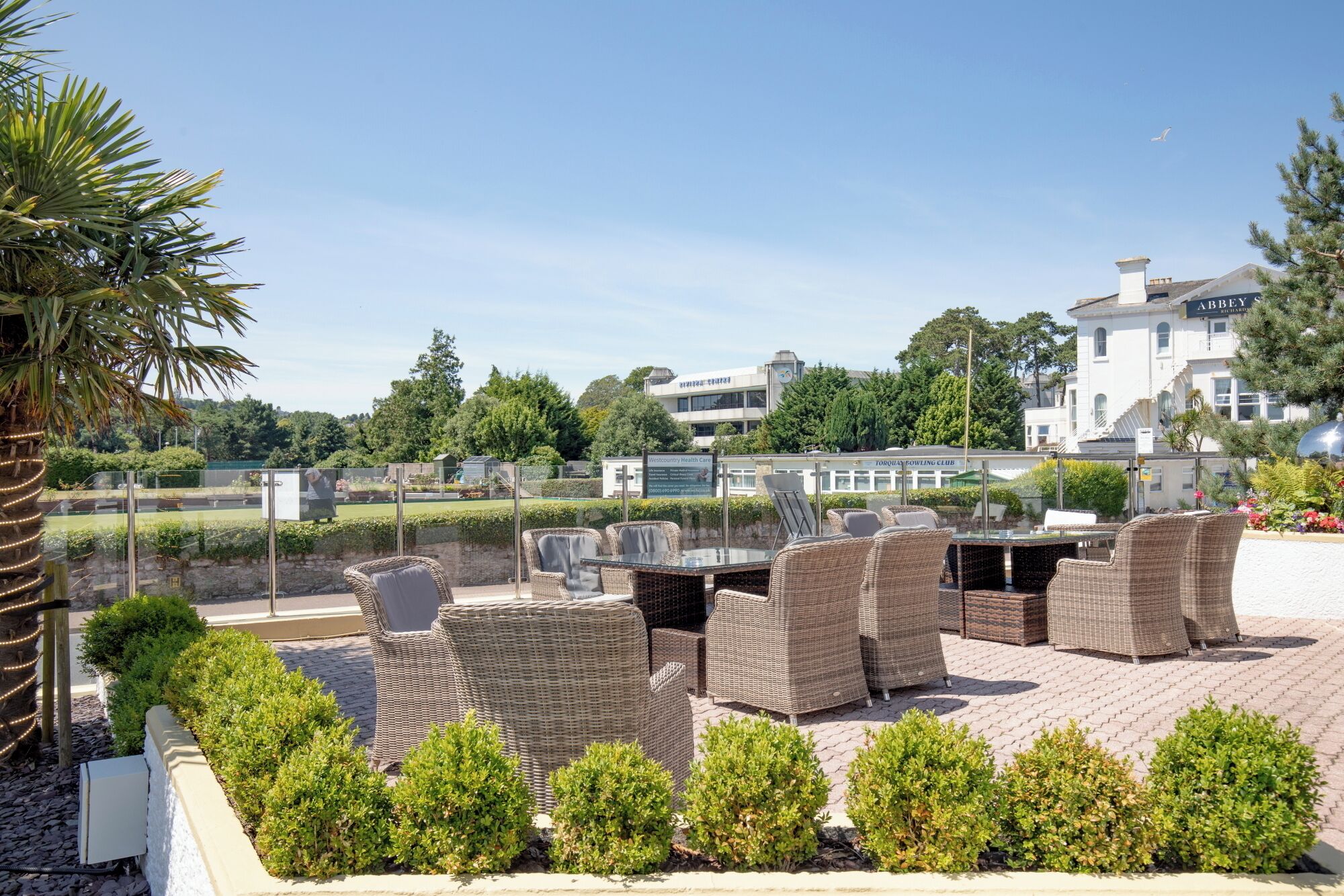Mobilier de jardin en osier, une terrasse dallée et une vue sur les bâtiments en arrière-plan.